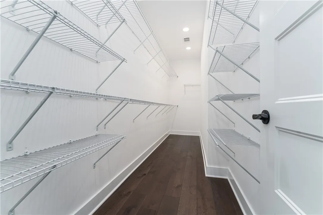 This spacious walk-in closet offers ample storage with convenient shelving and rich hardwood flooring.