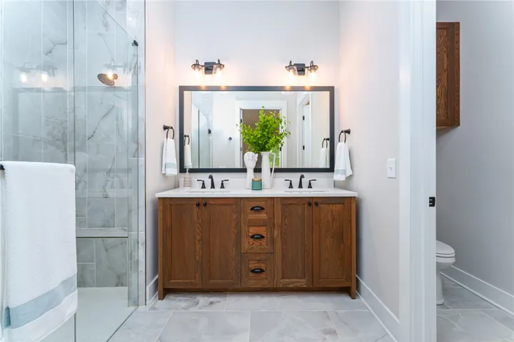 This bathroom features dual vanities and a tiled shower with a clear glass enclosure.