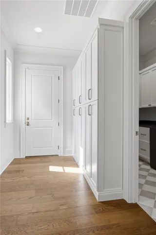 A hallway features warm wood flooring leading to built-in storage cabinets and a secondary room.