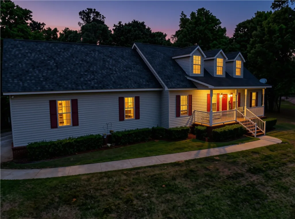 Illuminated windows and a welcoming front porch enhance this charming home at dusk.