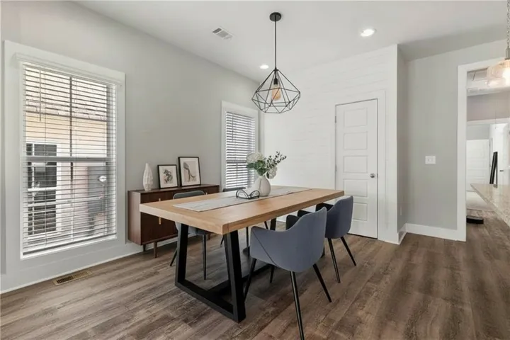 A spacious dining area features tall windows, clean moldings, and rich wood-texture flooring. Virtually staged.