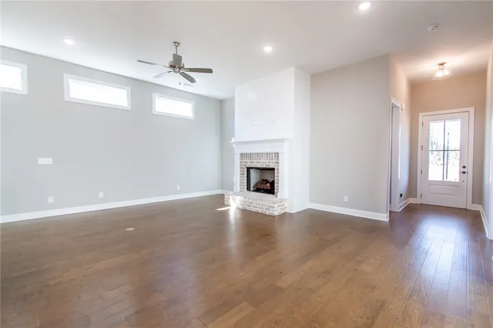 Bright and airy living area featuring a prominent brick fireplace and rich hardwood flooring.