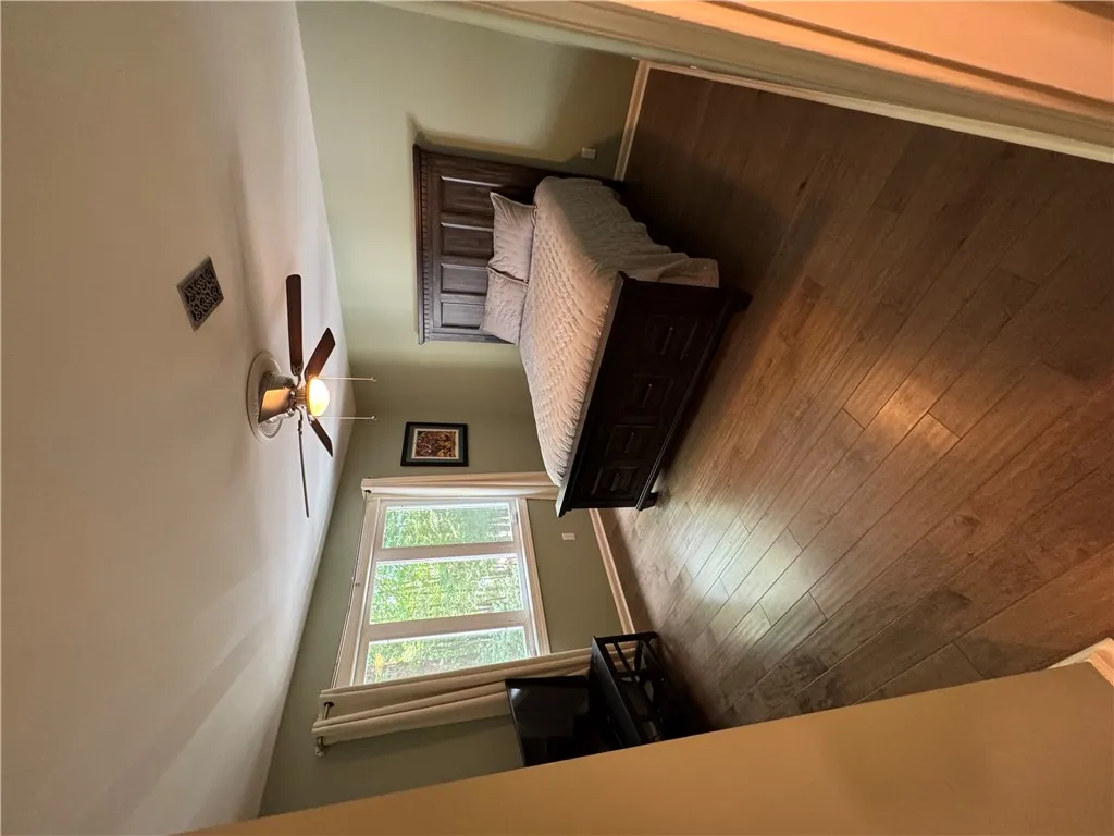 Comfortable sleeping space featuring rich wood flooring and abundant natural light from a broad window.