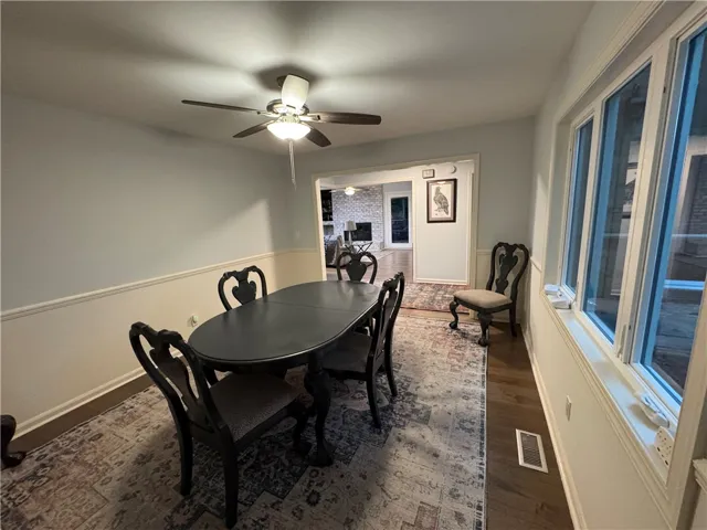 This formal dining space offers warm wood flooring, a decorative ceiling fan, and ample natural light from large windows.