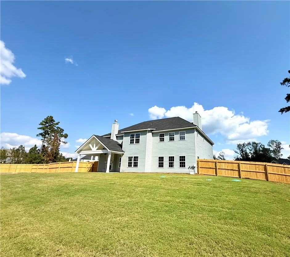 An expansive green lawn stretches behind this multi-story residence enclosed by secure privacy fencing.