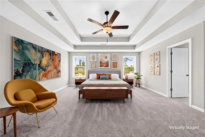 An elegant tray ceiling with crown molding crowns this spacious bedroom featuring plush wall-to-wall carpeting.