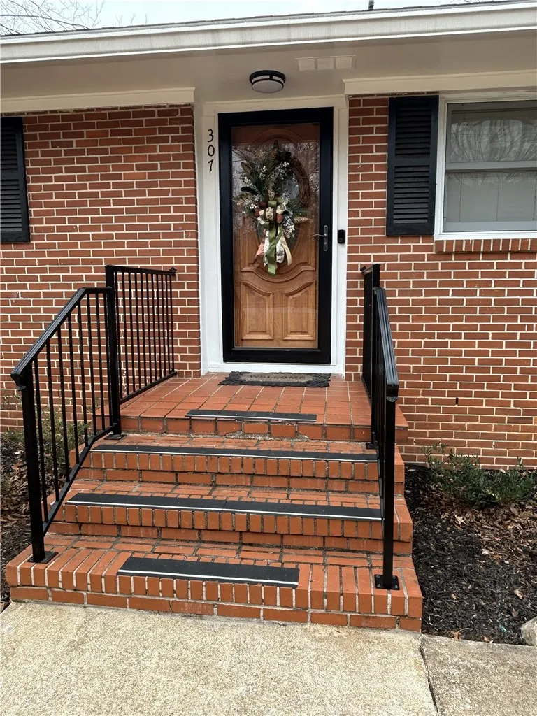 A classic brick facade welcomes with a polished wood entry door, featuring a sturdy handrail.