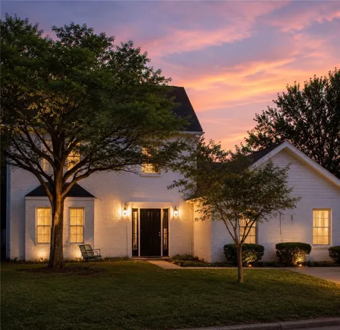 Illuminated by dusk's vivid hues, this residence features a striking dark entry framed by traditional brick and manicured landscaping.