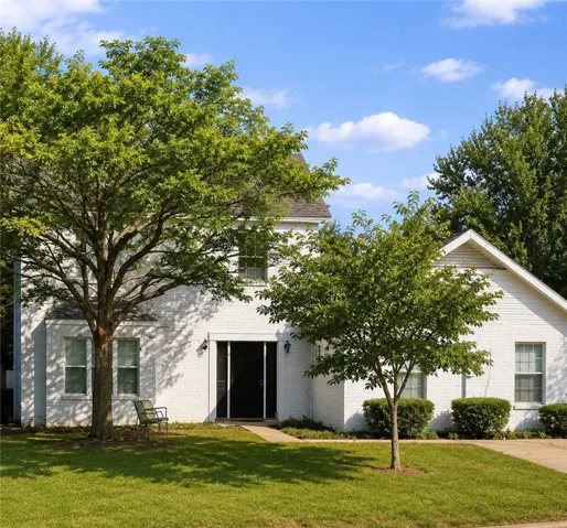 Timeless white brick home with mature shade trees on a verdant lot.