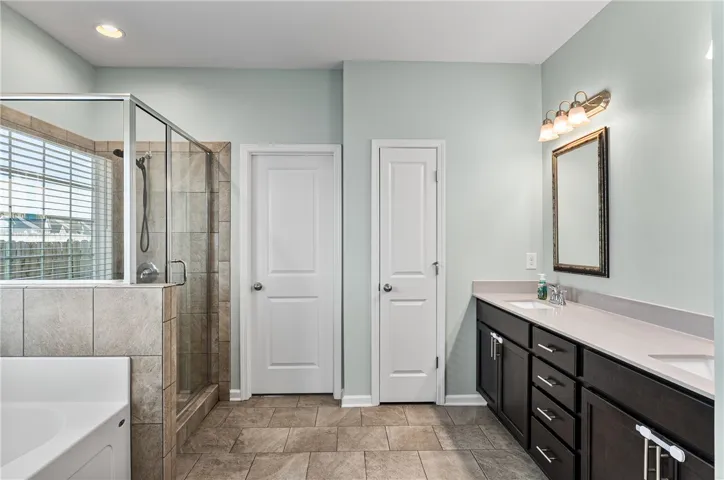 This spacious primary bathroom showcases a glass-enclosed shower, a large soaking tub, and a vanity with dual sinks.