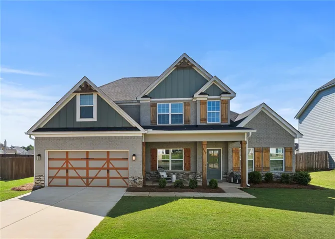 This two-story residence presents a welcoming facade with a charming covered front porch, brick and cement board exterior, and an attached garage.