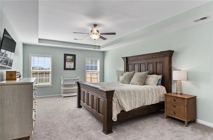This spacious primary bedroom features a striking tray ceiling and cozy carpeting, creating a serene retreat.