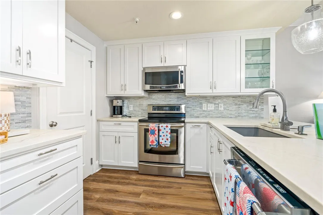 A well-lit kitchen features white cabinetry, stone countertops, and wood flooring for a fresh, functional aesthetic.