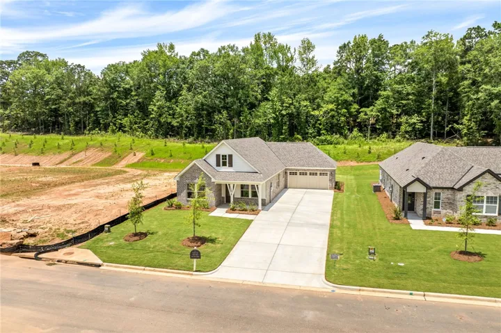 A newly constructed single-story home with a neat lawn and an attached garage, nestled among lush greenery.