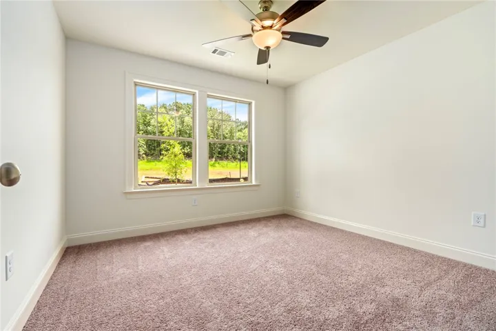 A tranquil bedroom features warm carpet and generous windows overlooking verdant trees.