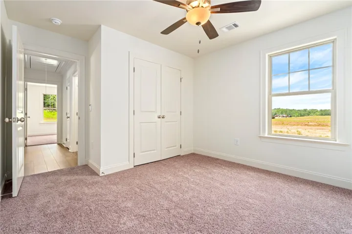 A well-lit bedroom features plush carpeting and a large window offering natural light.
