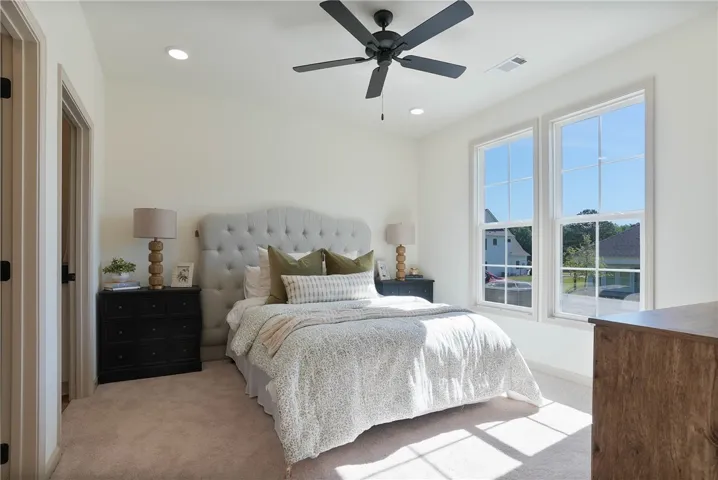Sun-filled bedroom featuring a tray ceiling, soft carpeting, and dual windows offering neighborhood views.