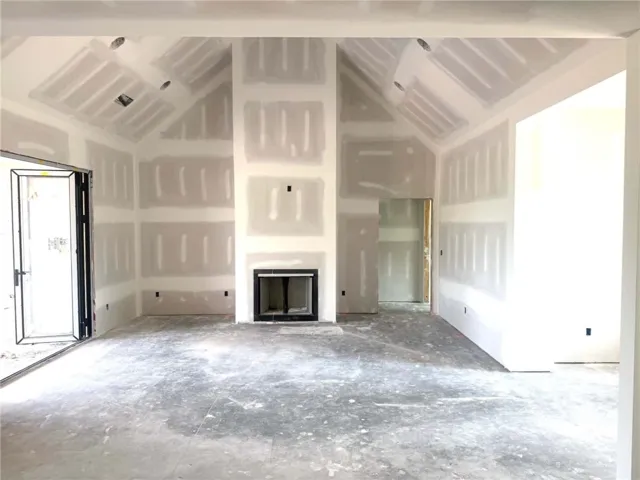 A spacious room under construction features a prominent fireplace and soaring vaulted ceilings.