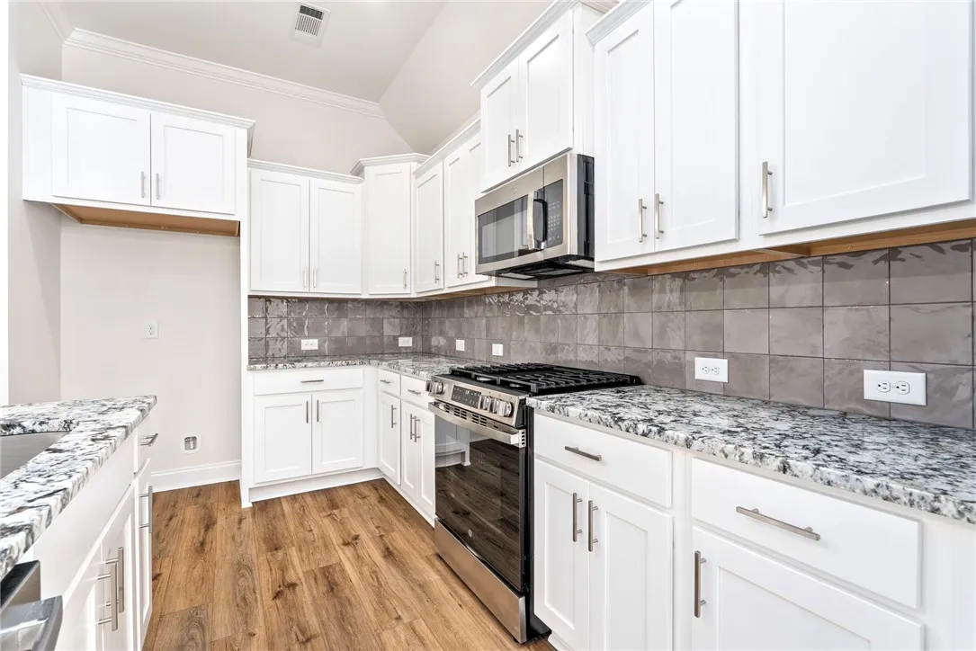 A well-appointed kitchen boasts sleek white cabinetry, granite countertops, and modern wood-look flooring.