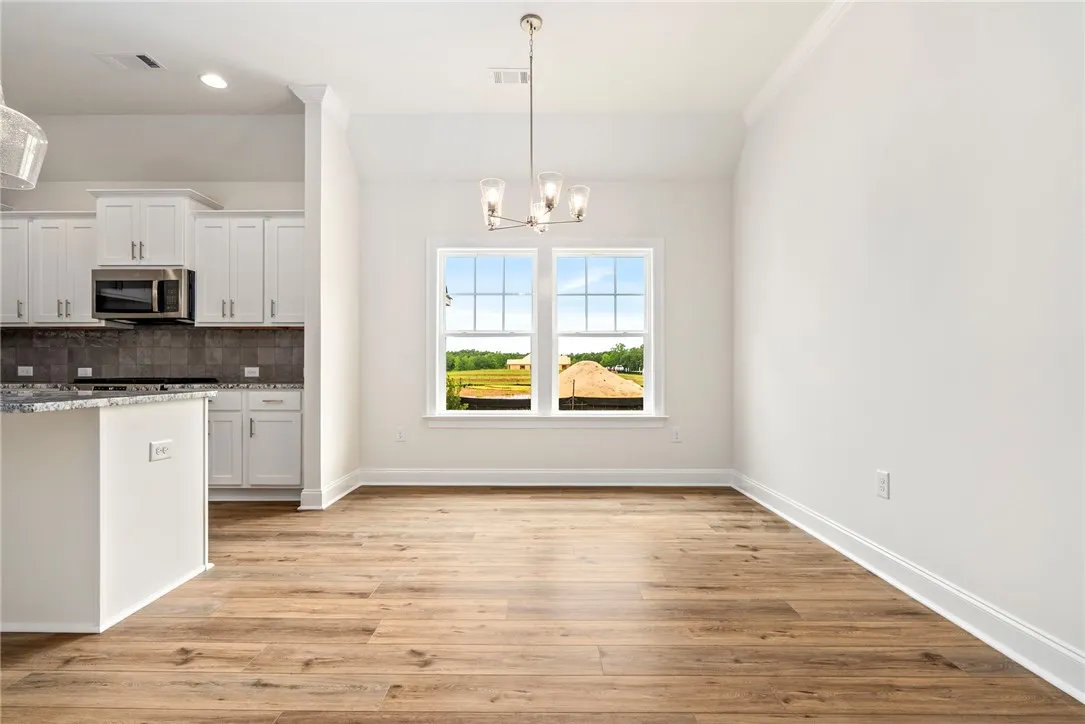 A well-lit dining area features durable hardwood-style flooring, a sleek light fixture, and an open layout to the kitchen.
