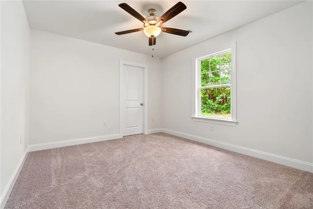 A spacious bedroom offers comfort with soft carpet and a cooling ceiling fan.