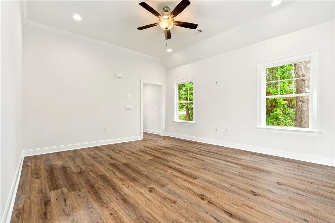 A welcoming, naturally illuminated living area featuring rich hardwood-style flooring and a contemporary ceiling fan.