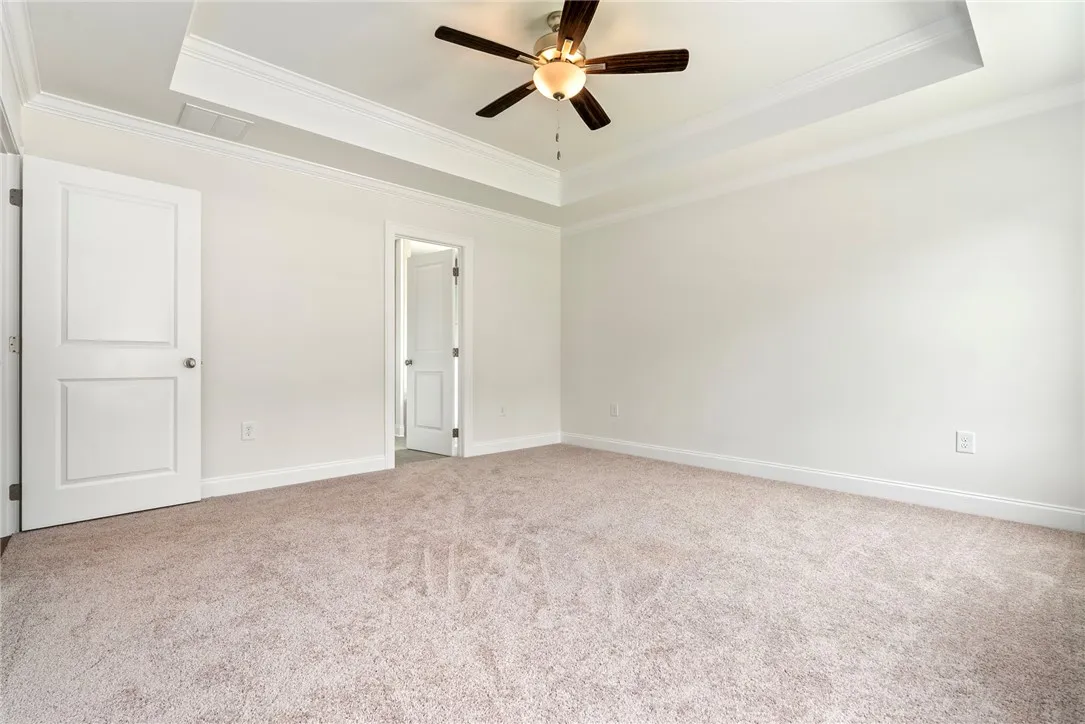 An inviting bedroom with plush carpeting features a tray ceiling and a ceiling fan.