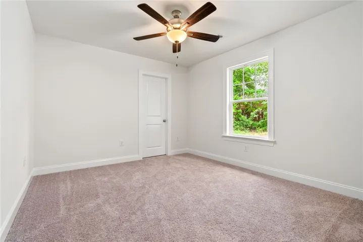 A spacious bedroom offers comfort with soft carpet and a cooling ceiling fan.