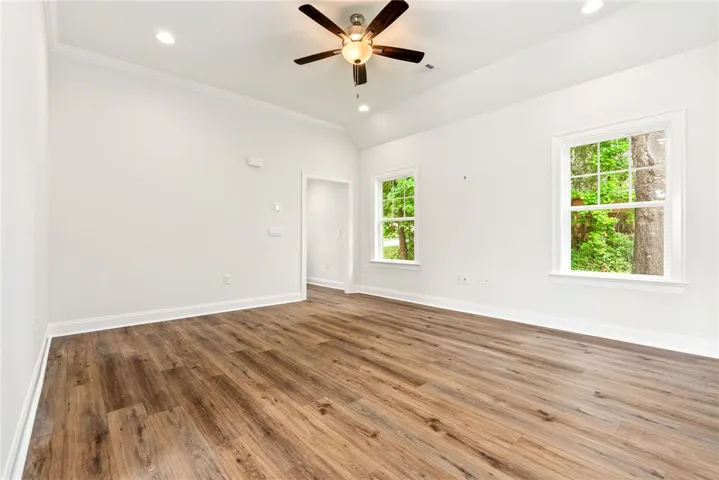 A welcoming, naturally illuminated living area featuring rich hardwood-style flooring and a contemporary ceiling fan.