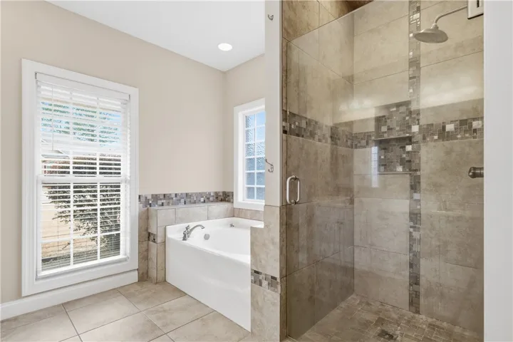Spacious primary bath offering a frameless glass walk-in shower, soaking tub, double-sink vanity, and linen storage.