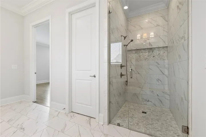 Spa-inspired frameless glass walk-in shower featuring oversized marble-look tile, a designer mosaic accent band, a built-in bench, and a recessed shampoo niche for a sleek, custom finish.