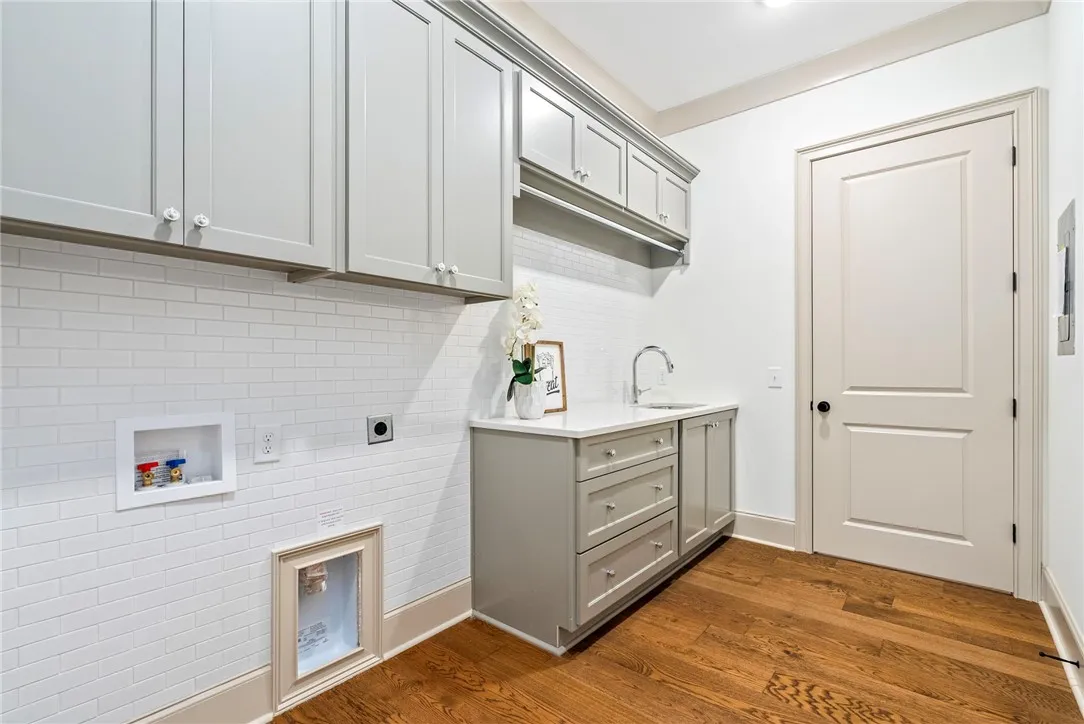 Functional laundry room featuring abundant cabinet storage, a practical sink, and rich hardwood flooring right off the Master Closet.
