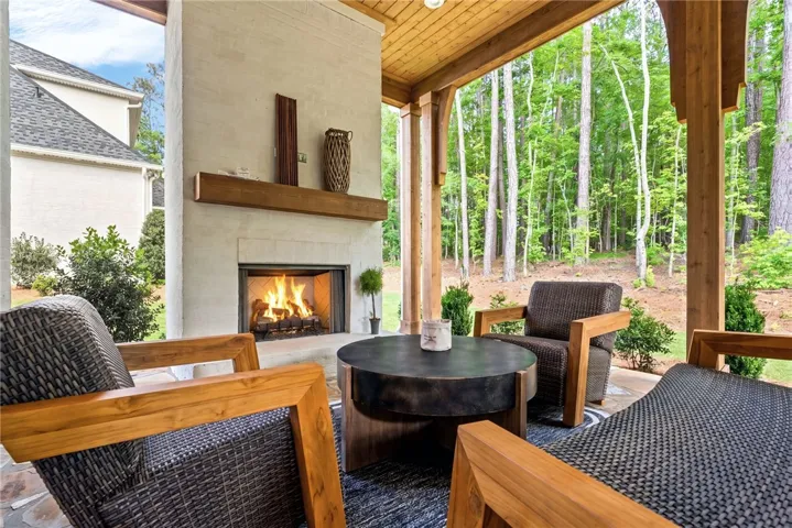 A spacious outdoor patio features a cozy fireplace and overlooks a serene woodland landscape.