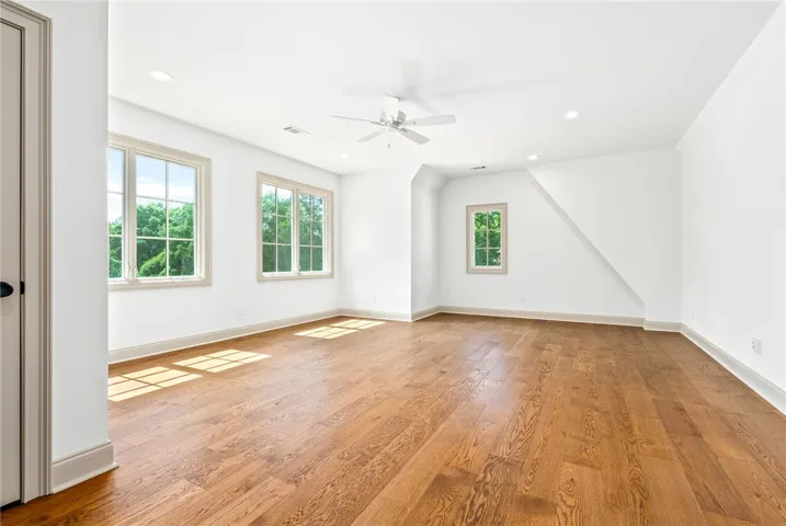 Naturally illuminated, this spacious bedroom features gleaming hardwood floors and ample window views of the verdant surroundings.