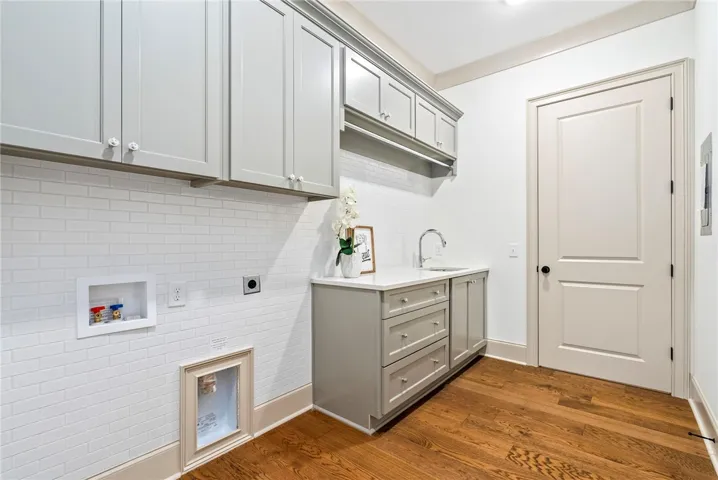 Functional laundry room featuring abundant cabinet storage, a practical sink, and rich hardwood flooring right off the Master Closet.