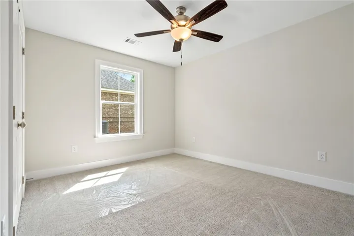 A window-lit room offers comfort with a ceiling fan and carpeted flooring.