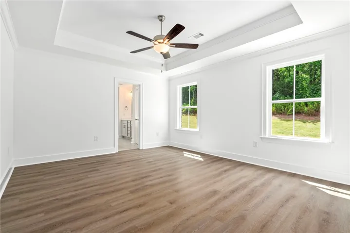 A spacious primary bedroom with warm-toned hardwood flooring and a recessed ceiling features ample natural illumination.