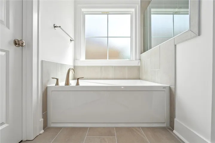 A well-lit soaking tub offers a serene escape, complemented by contemporary tiling and frosted window.
