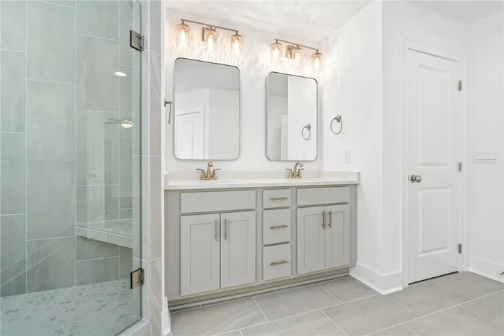 A chic bathroom offers dual vanities and a spacious walk-in shower with tiled walls.
