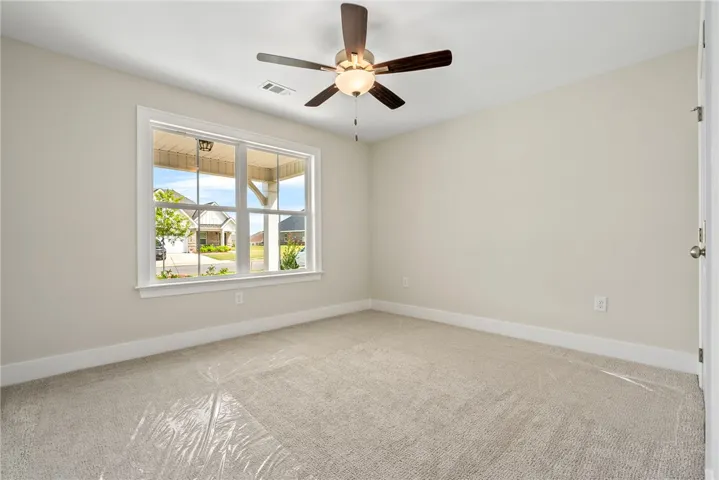 A well-lit bedroom features plush carpeting and a modern ceiling fan, offering comfortable living.