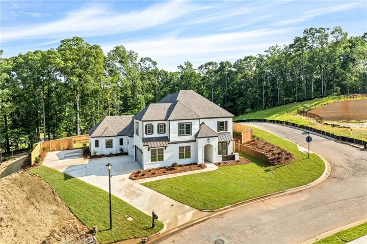 A striking white residence boasts modern black accents, a well-manicured lawn, and a spacious driveway on a curving street.