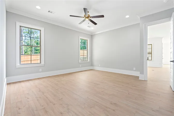 A tranquil primary bedroom with ample light, featuring light wood flooring and a contemporary ceiling fan.