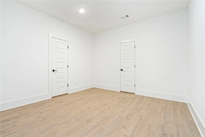Recessed lighting illuminates this room, complemented by light wood flooring and clean white walls.
