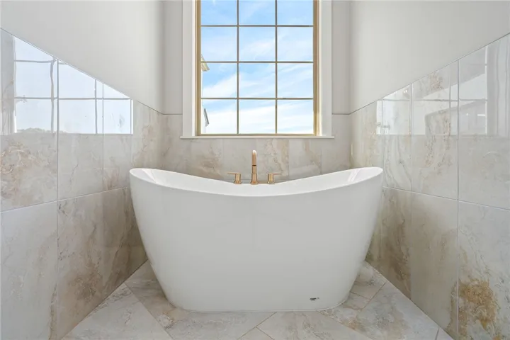 Indulge in relaxation with a freestanding soaking tub set against a backdrop of natural stone tile.