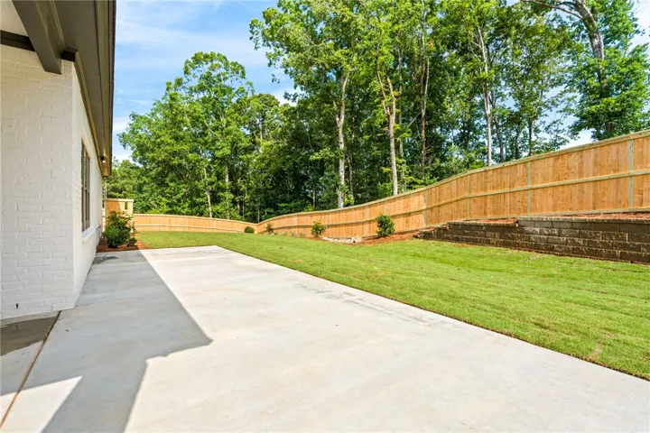 A spacious concrete patio adjoins a grassy yard, enclosed by a privacy fence with a lush tree line beyond.