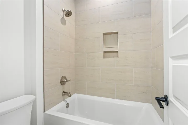A well-appointed bathroom offers a clean tub and tiled shower with a built-in niche.