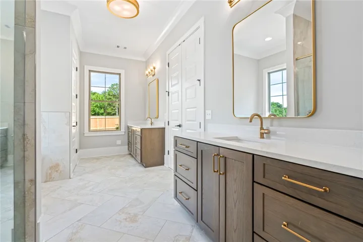 Dual vanities with golden fixtures and mirrors define this generously proportioned primary bathroom.