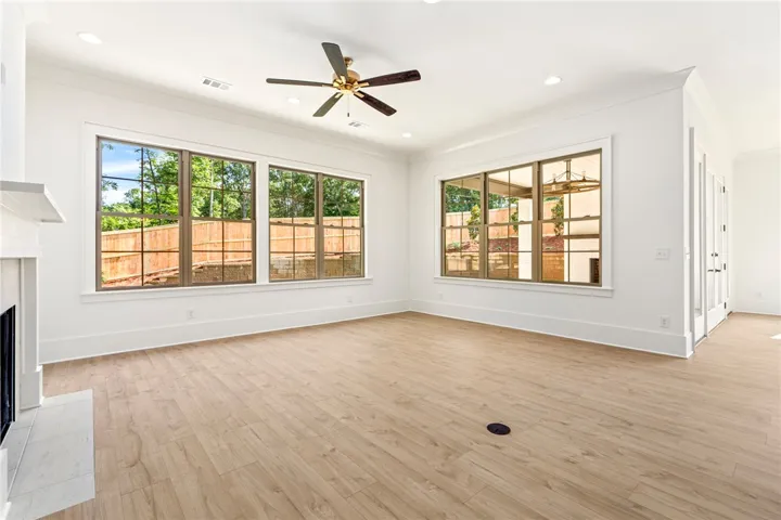 A spacious living area with abundant natural light, showcasing light-toned wood flooring and a classic ceiling fan.