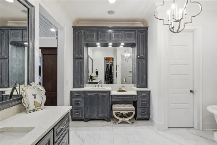 Dual vanities with abundant cabinetry—including a seated dressing area—are framed by full-height mirrors and tailored lighting, creating a polished and highly functional bath space.