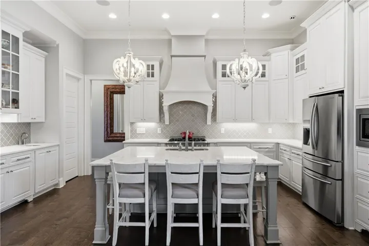 Tall cabinety with glass-front accents set the tone for the kitchen, where a generous island, custom hood, gas range, wet bar, and oversized pantry provide both style and everyday practicality.